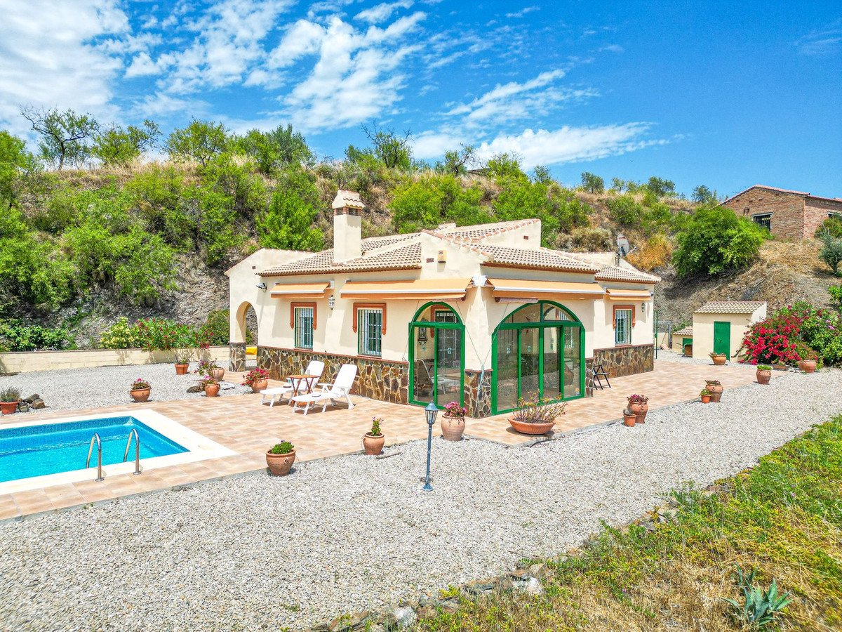 Villa with a swimming pool, patio, and garden on a sunny day. Features a glazed porch and hillside views.