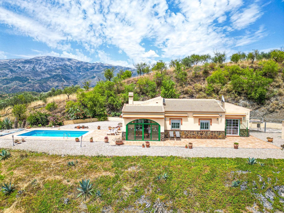 A traditional villa with a swimming pool and terrace, set against a backdrop of mountains and lush greenery.
