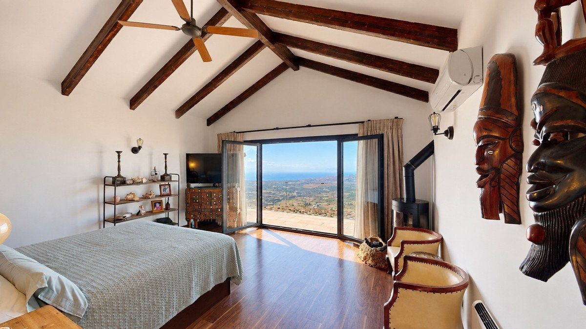 Bedroom with a beamed ceiling, large windows offering an ocean view, and decorative wooden masks on the wall.