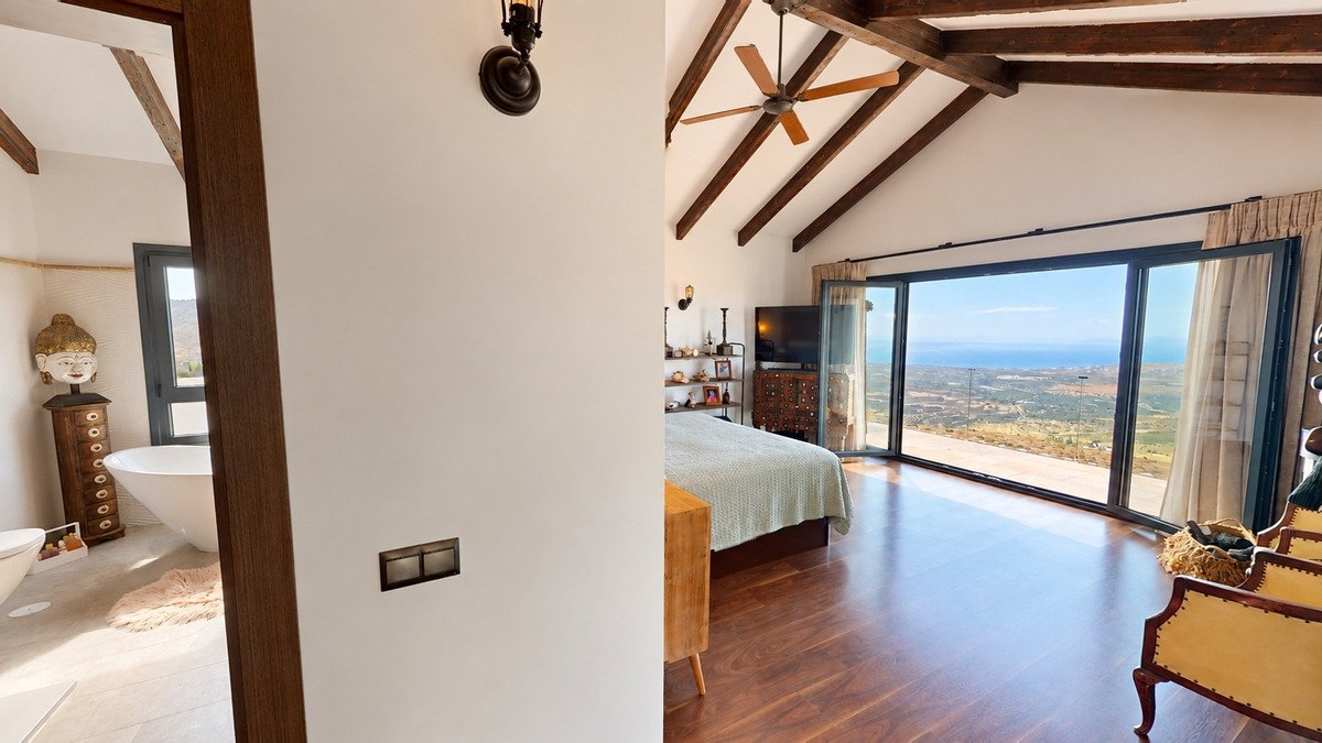 Bedroom with a large bed, TV, and a stunning ocean view through sliding glass doors. Adjacent bathroom with a freestanding tub.
