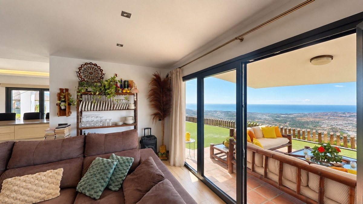 Living room with a large sofa opening onto a terrace with a sea view and outdoor seating.