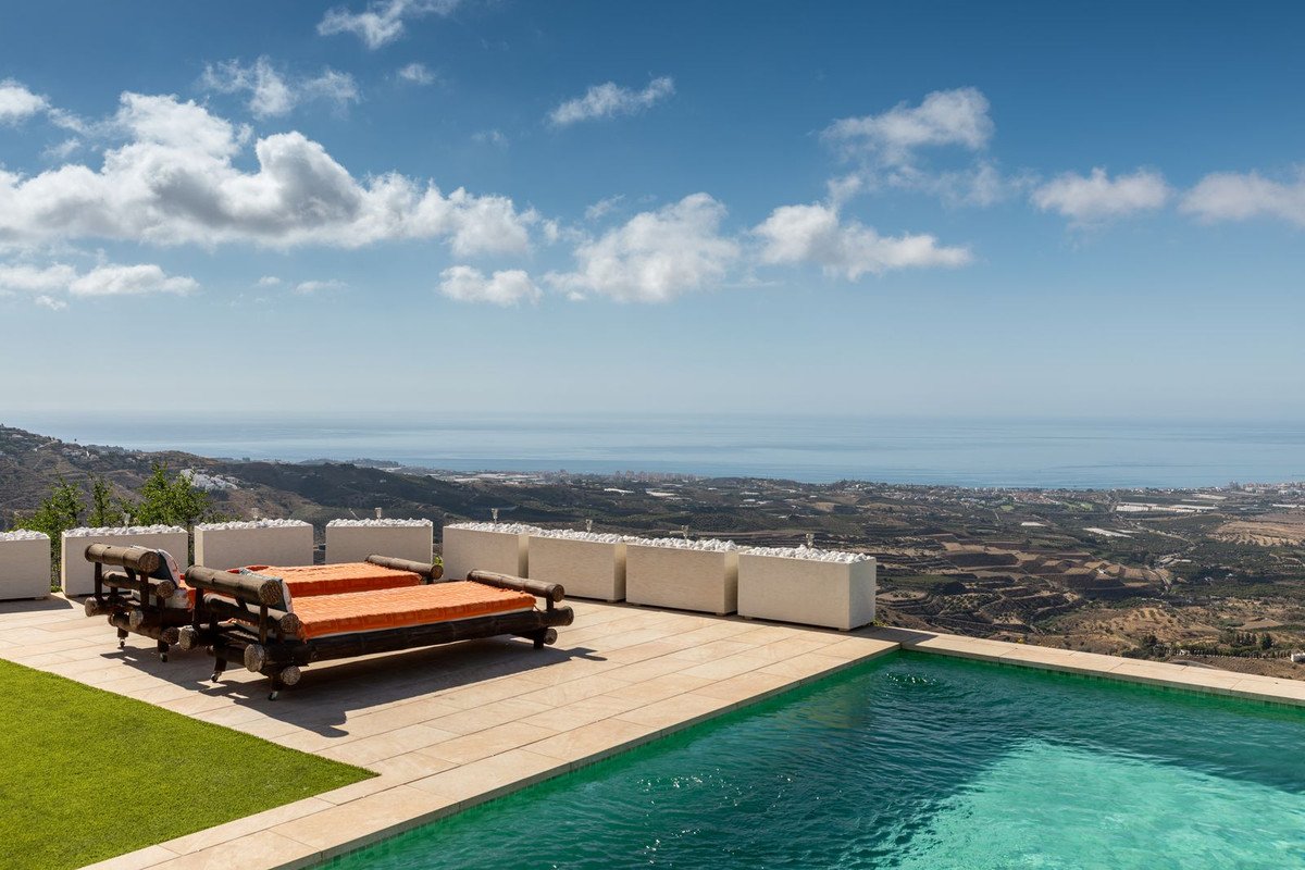 Luxurious outdoor lounge area with pool and sunbeds overlooking the sea and rolling hills.