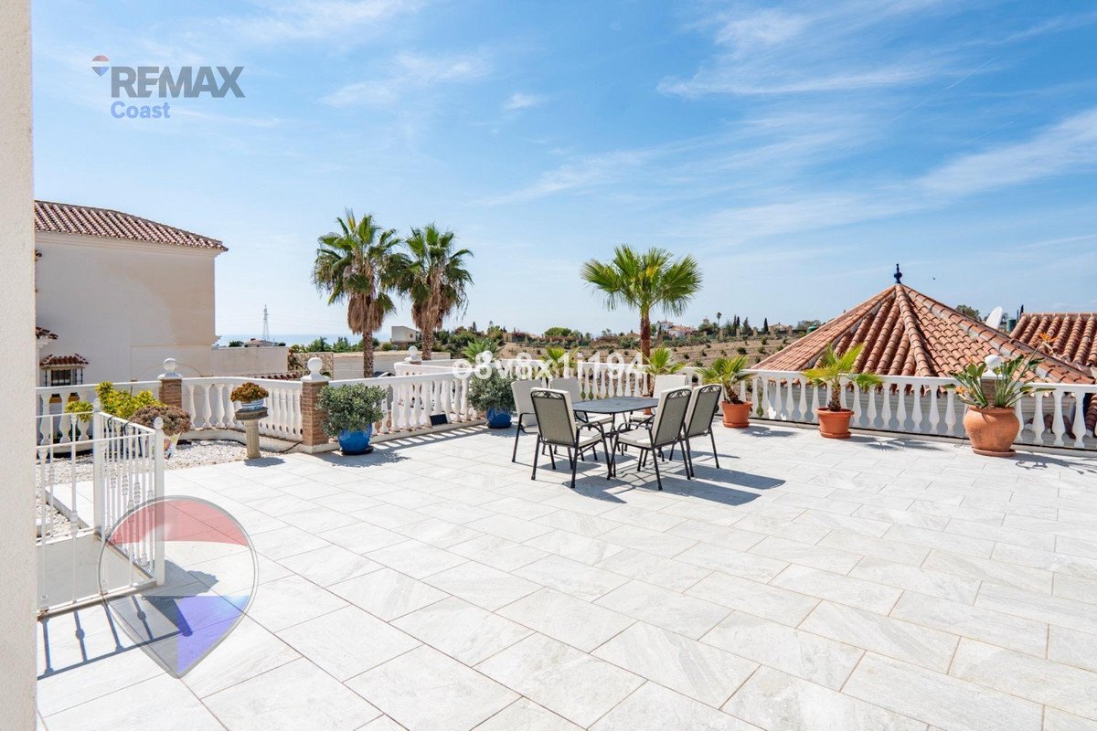 Spacious terrace with seating area, palm trees, and a distant view of the sea under a clear blue sky.