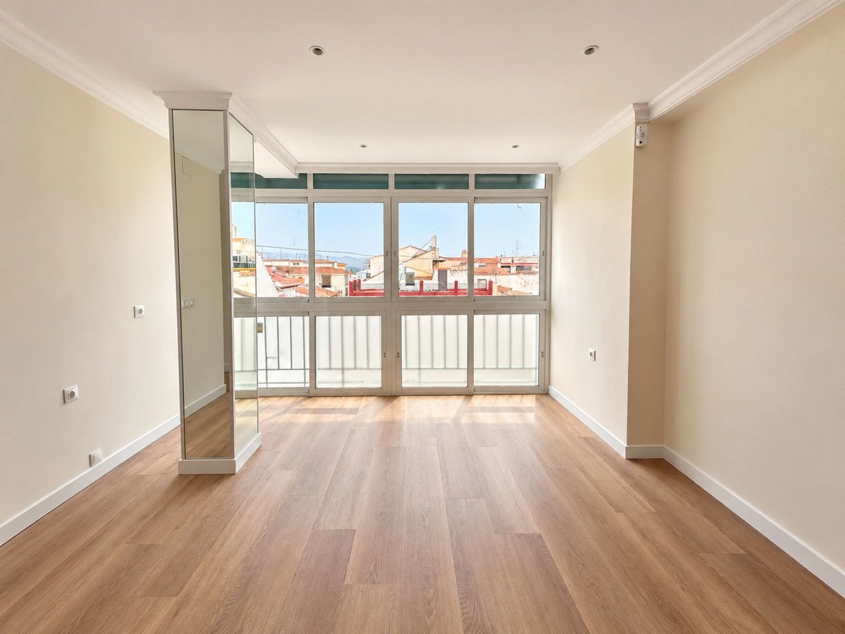 Empty living room with large windows offering a city view. Features a mirrored column and wooden floors.