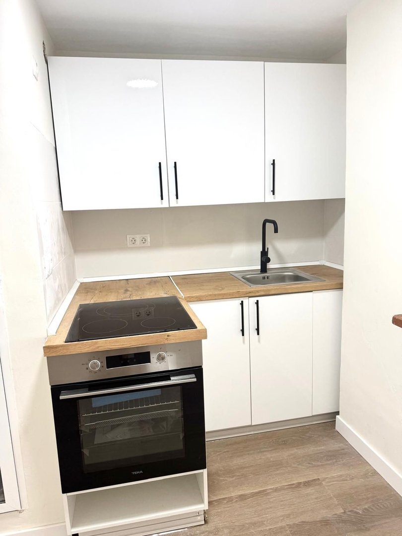 A modern kitchen with white cabinets, induction hob, oven, sink, and wooden countertops.