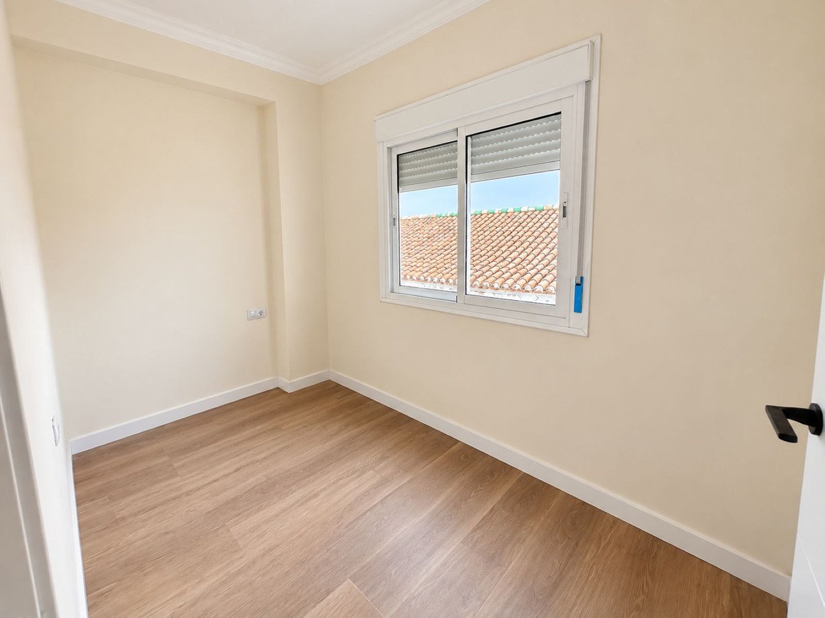 Empty room with cream walls, wooden floors, and a window overlooking tiled rooftops and the sky.