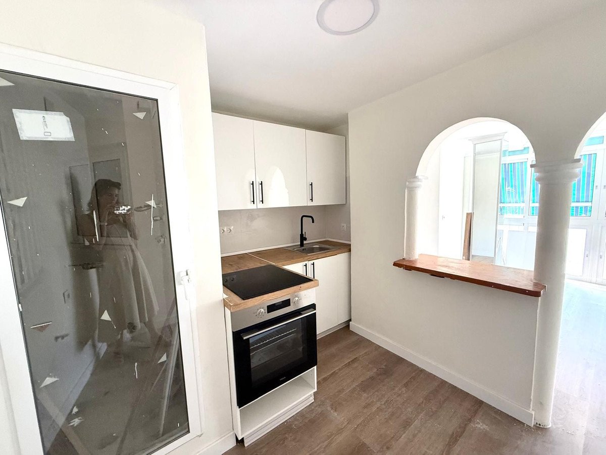 A modern kitchen with white cabinets, an oven, and a breakfast bar opening to another room.