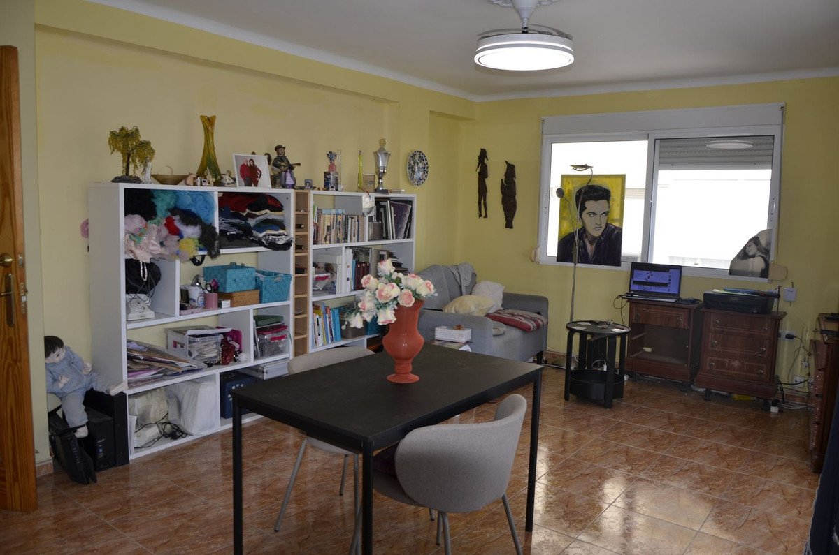 A living and dining room with a bookshelf, couch, and a dining table in the center, decorated with a portrait of Elvis Presley.