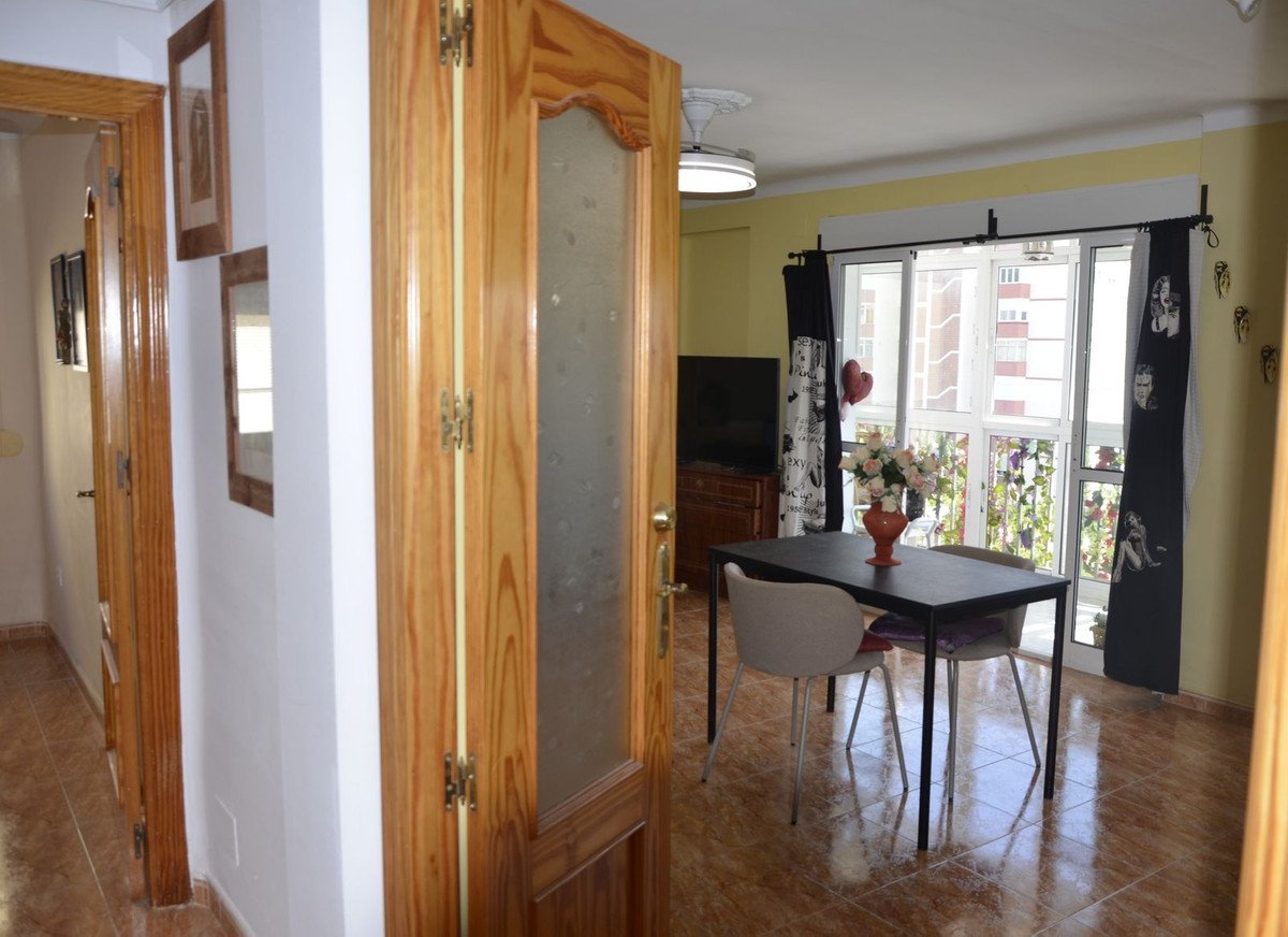 Dining area with a table and chairs, overlooking a balcony with plants and city buildings. Curtains feature vintage portraits.