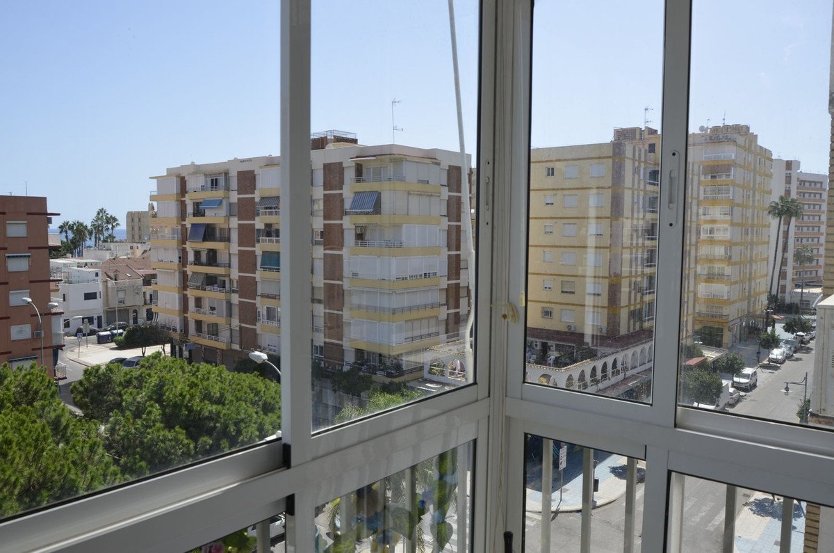 View from a balcony overlooking city buildings, trees, and a street with cars under a clear blue sky.
