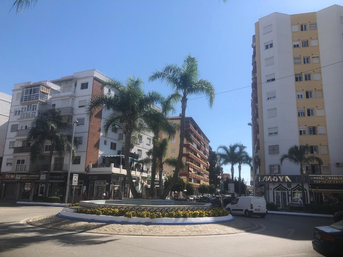 View of urban street with apartment buildings, palm trees, and a roundabout with a fountain on a sunny day.