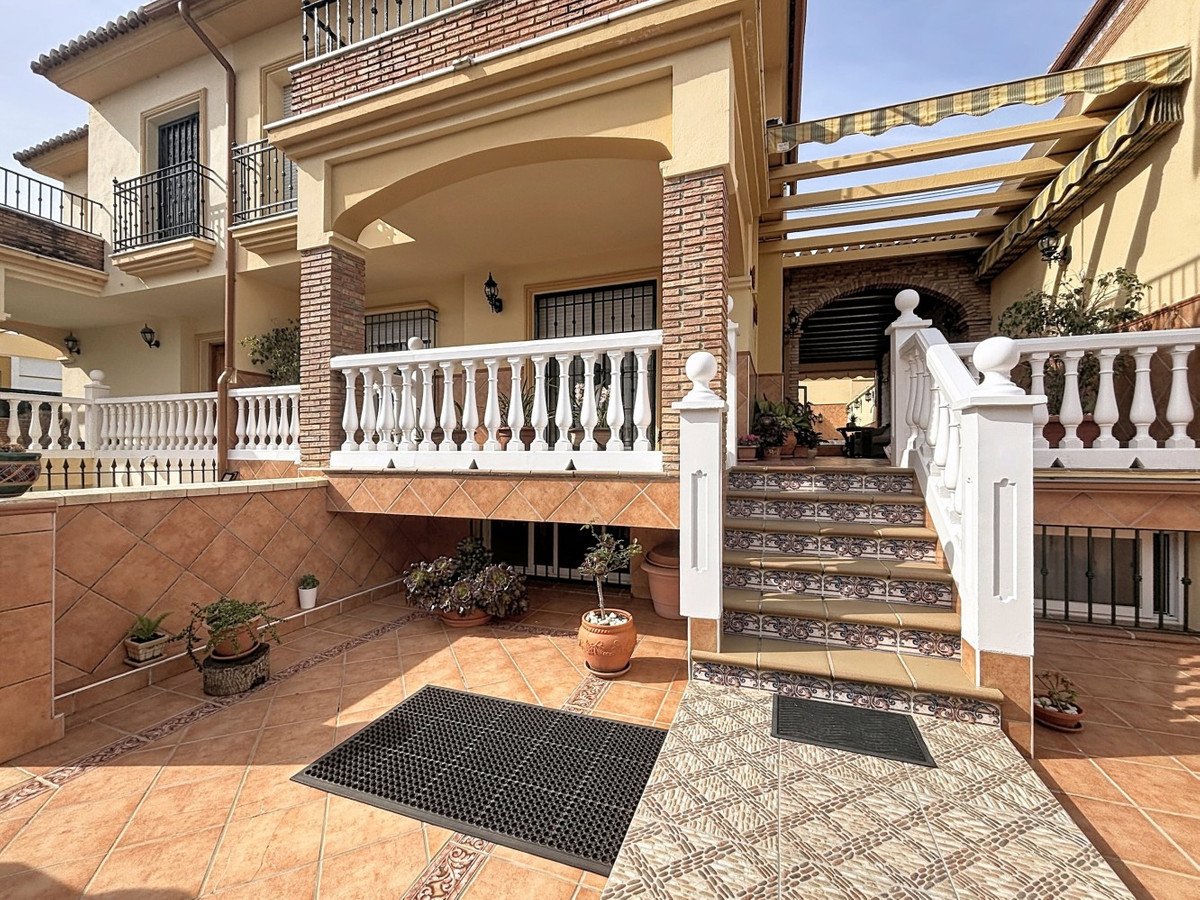 Terraced house with a tiled patio, white balustrades, decorative steps leading to an arched entryway, and balconies.