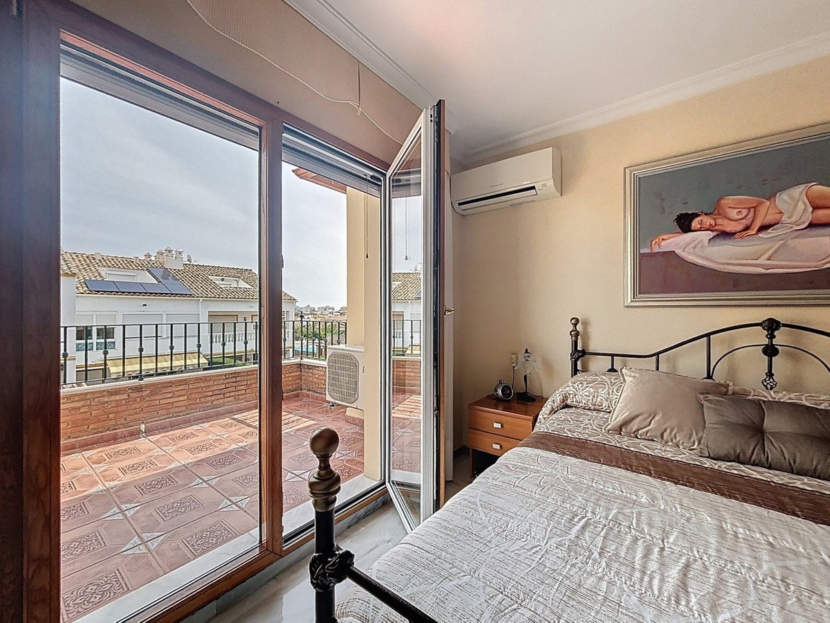 Bedroom with a bed and a large glass door opening to a terrace with rooftops and solar panels visible. Air conditioning unit is present.
