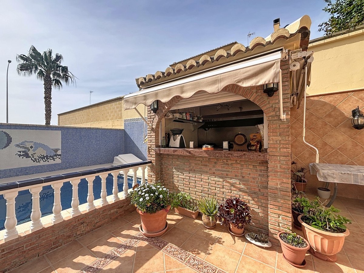 Outdoor brick bar with a pool view, featuring a palm tree and potted plants on a sunny day.
