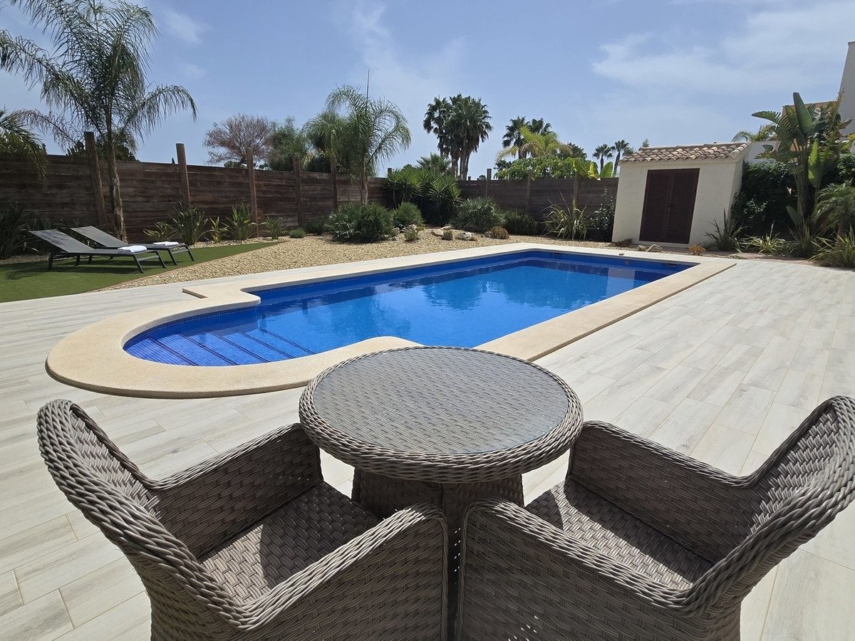 A private swimming pool with blue water, surrounded by a tiled patio, loungers, and lush greenery under a sunny sky.