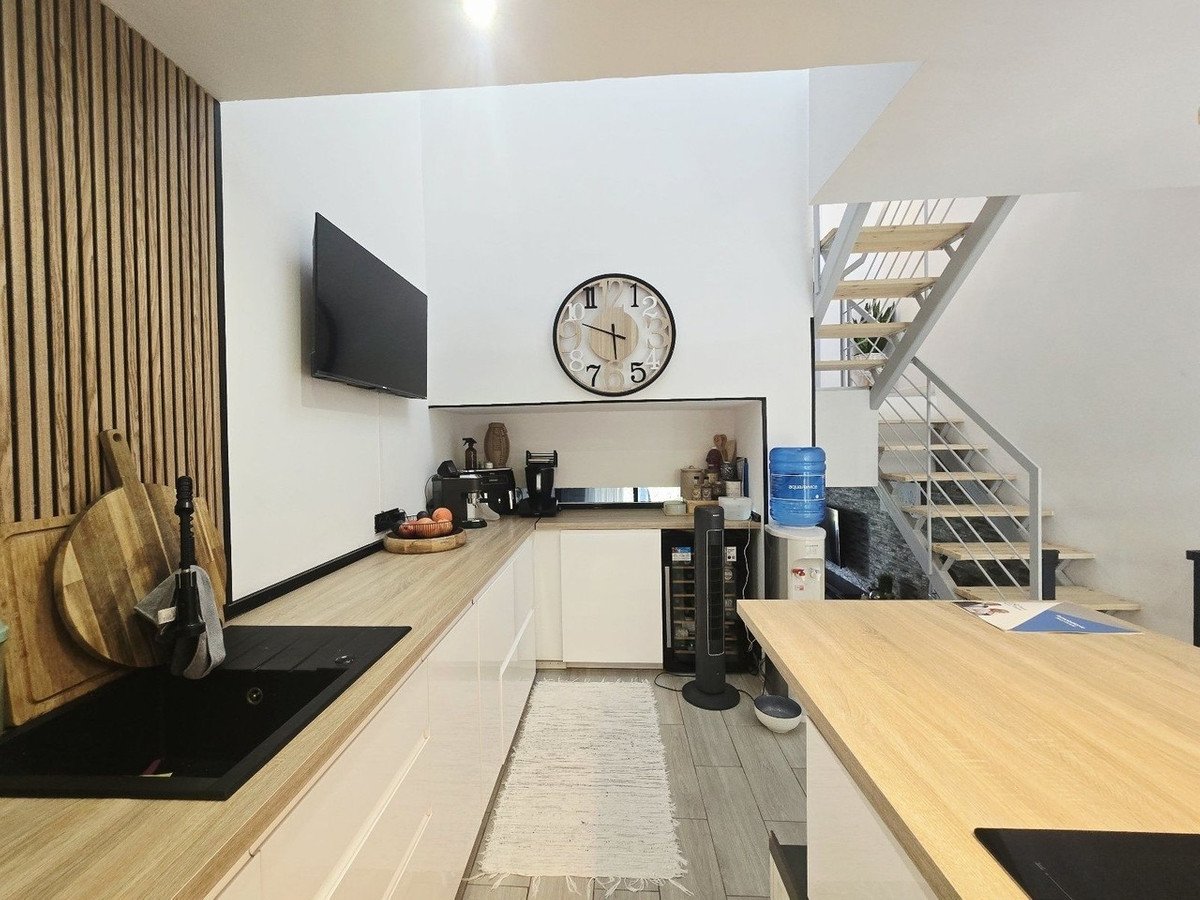 Modern kitchen with light wood counters, black sink, and staircase in background