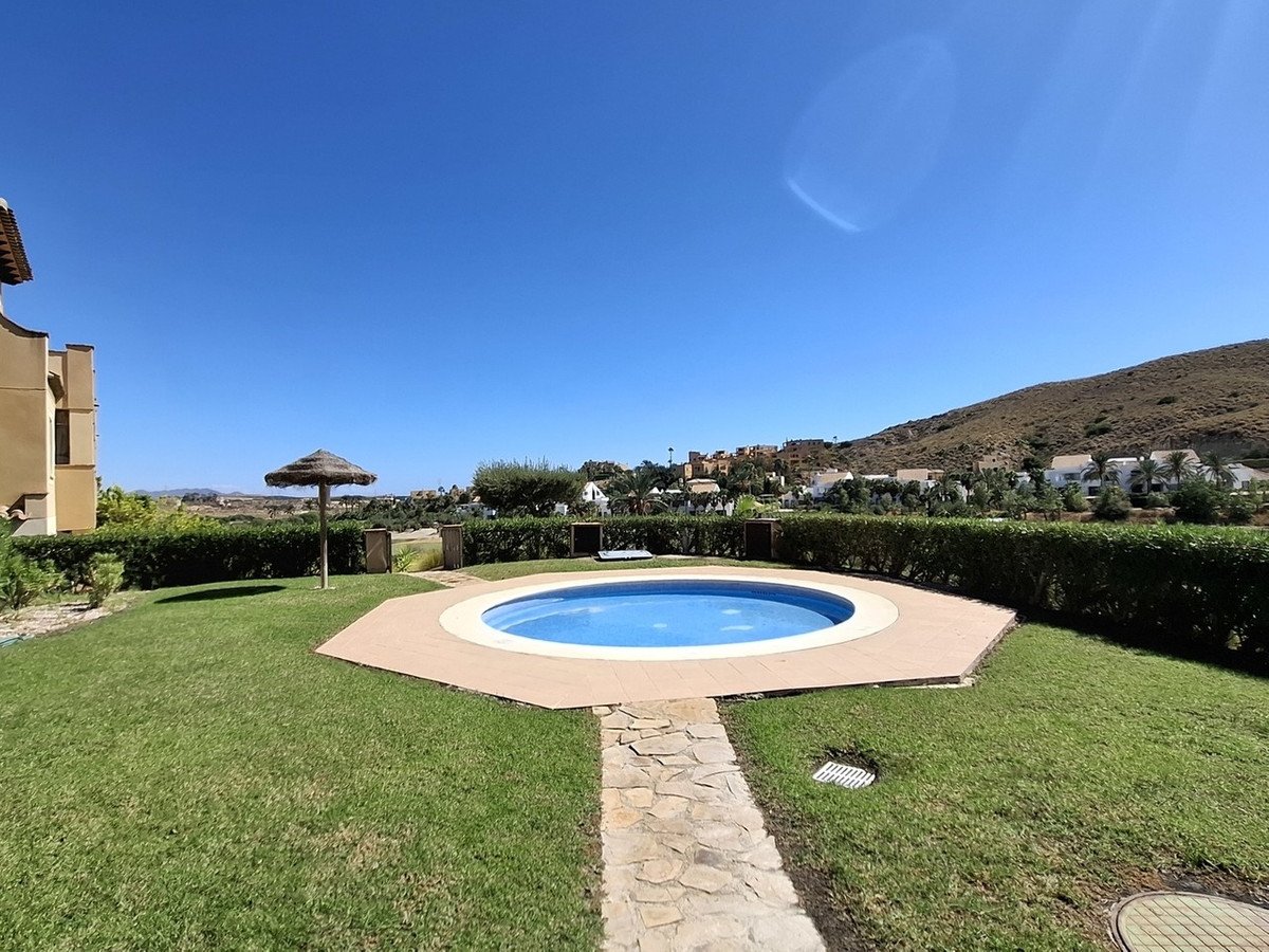 A private pool with a thatched umbrella and manicured garden, set against a backdrop of hills and houses under a clear blue sky.