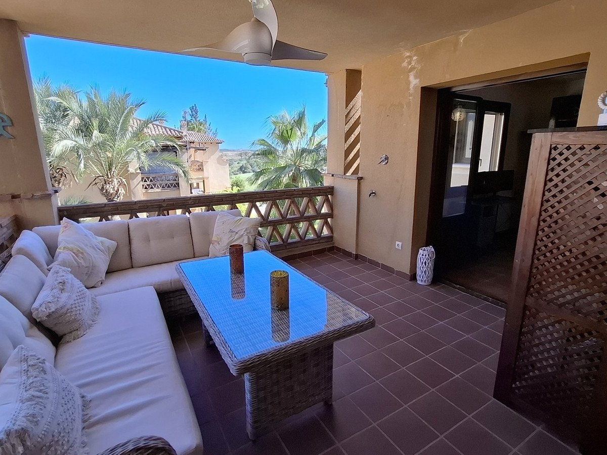 A spacious covered terrace with a large L-shaped sofa, glass-top coffee table, and views of palm trees and buildings.