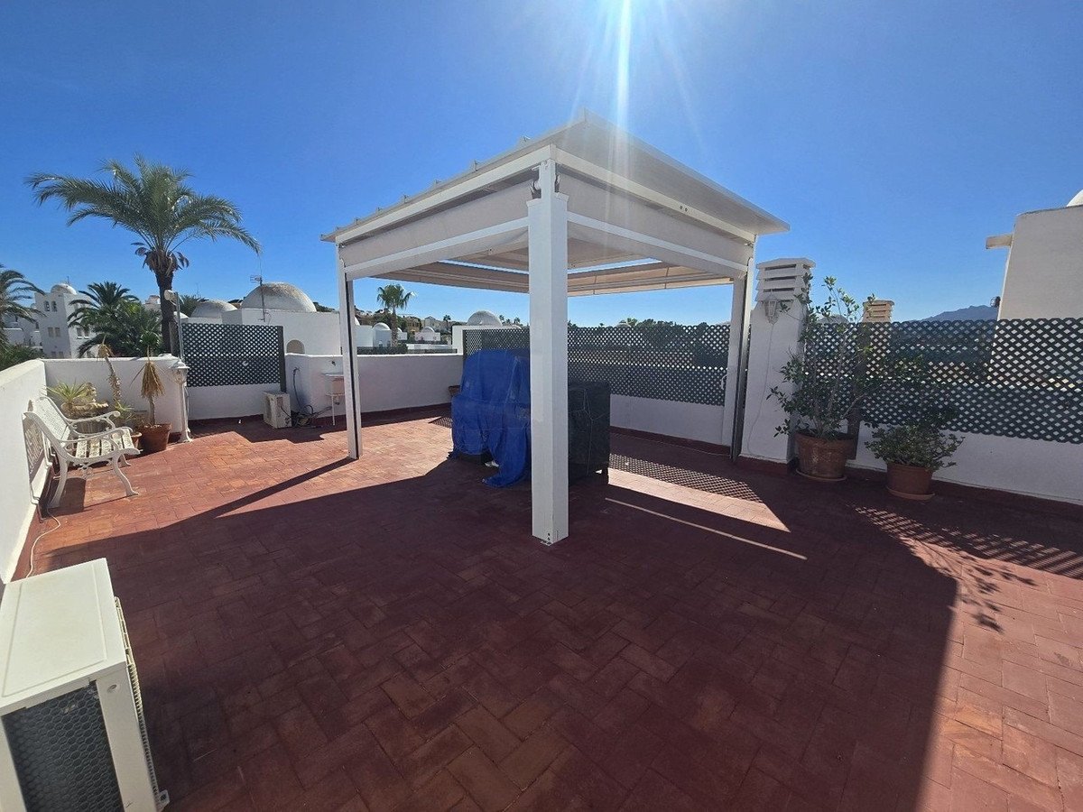 Rooftop terrace with pergola, brick flooring, and outdoor seating under sunny sky