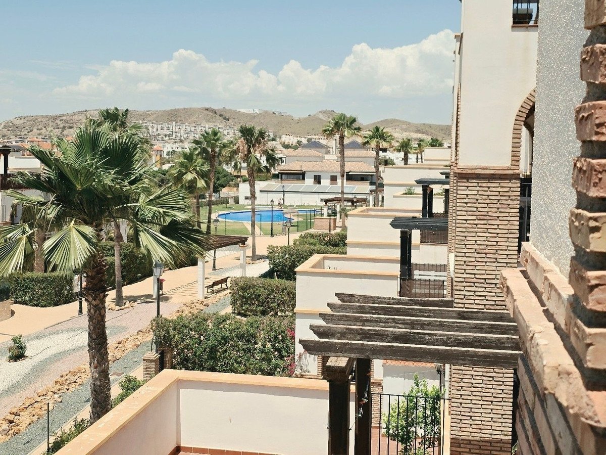 Apartment balcony overlooking a swimming pool with palm trees and surrounding buildings.