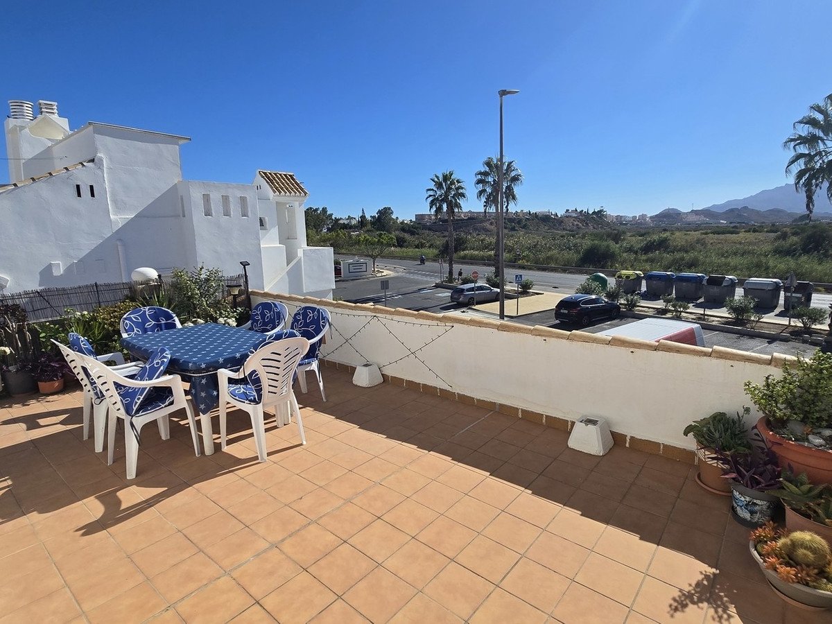 Terrace with a table and chairs, overlooking distant mountains and palm trees under a clear blue sky.