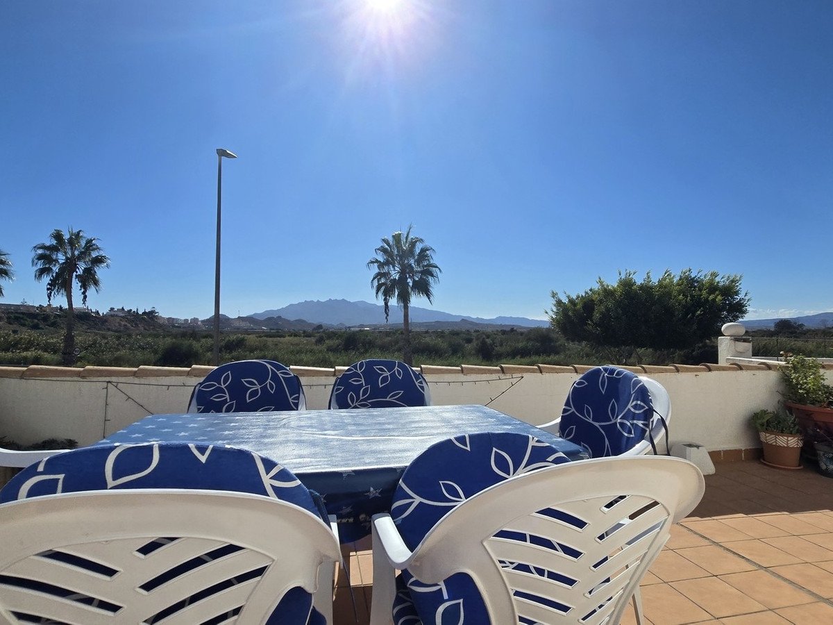 Outdoor dining table and chairs on a sunny terrace with palm trees and mountain views.