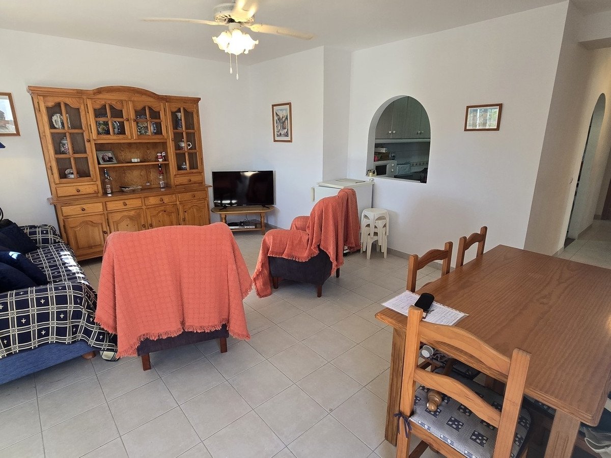 Interior of a living and dining room with wooden furniture, sofa, chairs, dining table, and a glimpse of the kitchen.