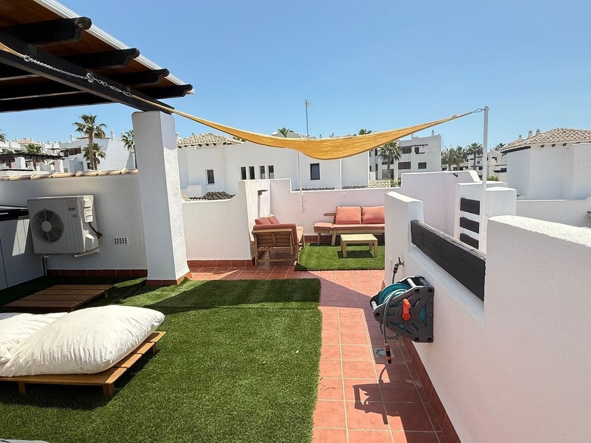 Rooftop terrace with sunshade, seating, artificial grass, and white buildings in background