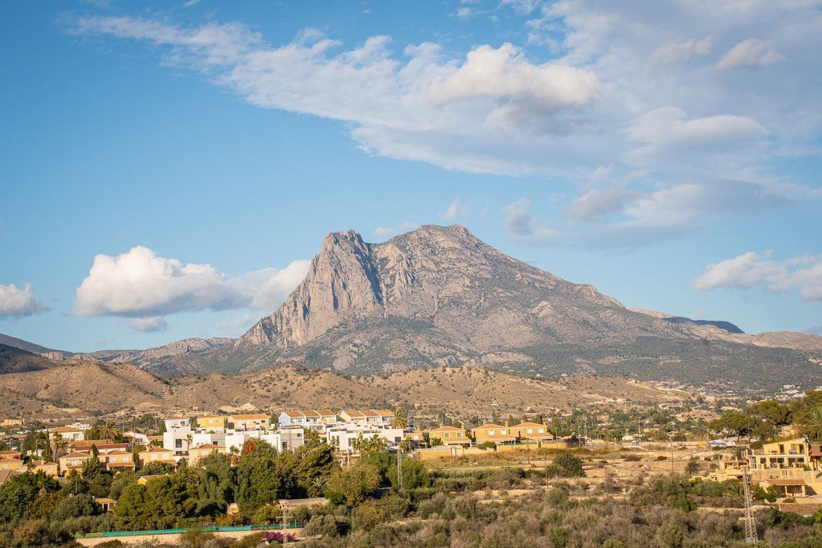 A scenic view of houses nestled in a valley with a large, imposing mountain in the background under a blue sky.