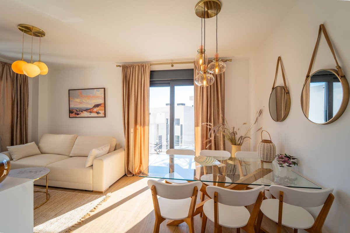 Modern living and dining area with a cream sofa, glass dining table, and large windows with golden curtains.