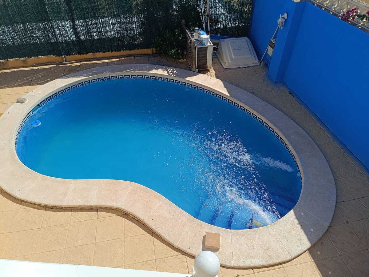 A clear blue outdoor swimming pool with a tiled surround and a blue wall in the background.