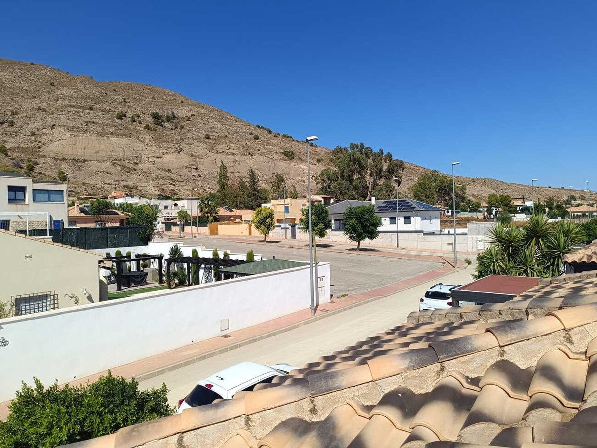 View of a residential area with houses, a street, and a mountain in the background under a clear blue sky.