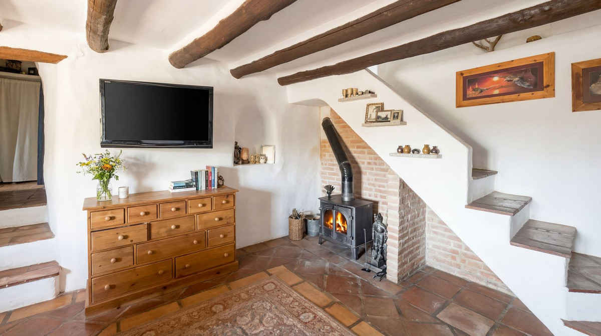 Rustieke woonkamer met open haard, houten balken en stenen vloer.