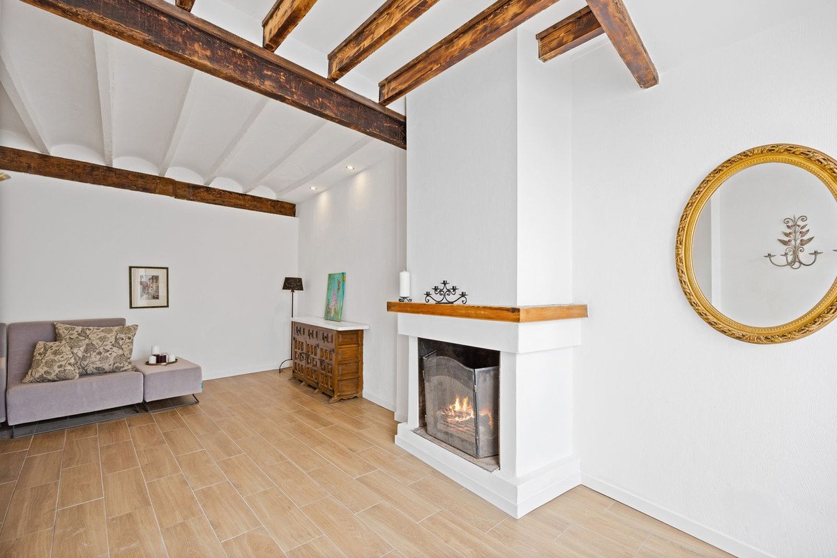Living room with a fireplace, wooden beams on the ceiling, a sofa, and a decorative dresser.