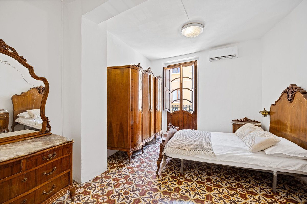 A bedroom with antique wooden furniture, a large ornate mirror, and a balcony door opening to a street view.