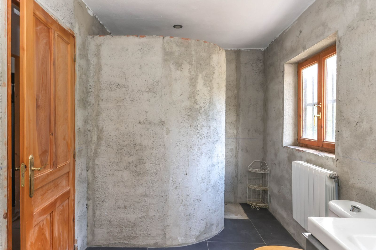 Badkamer in renovatie met ruwe muren, houten deur en raamkozijn.